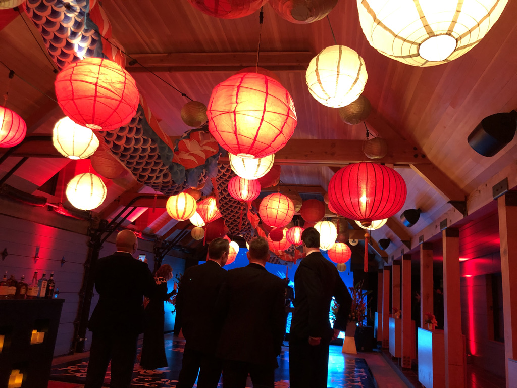Guys in fancy suits watching a dancefloor in a very fancy garage with red paper lanterns